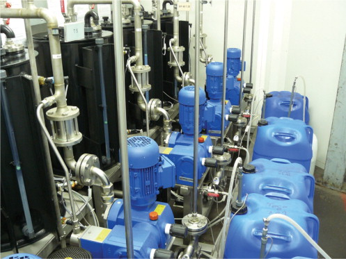 Figure 2a. The centralized coating preparation: (L-R) supply tanks (black); four of the five Bran+Luebbe metering/mixing pumps; coating agent containers (blue).